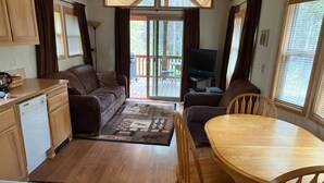 A compact kitchen with a stove, a dining area with a table and chairs, a sofa, and a television. - Young at Heart Chalet, Pet Friendly- 507 (Crescent Lake Junction)