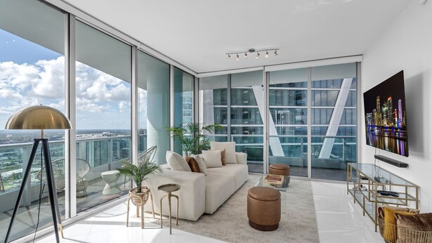 Un salon moderne avec un grand canapé, une table basse, un téléviseur et un balcon offrant une vue sur la ville.