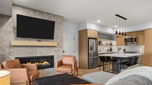 A modern living room with a fireplace, leather sofas, and a flat-screen TV mounted on a stone wall. - “The Ascent Mountain Haven” (Canmore)