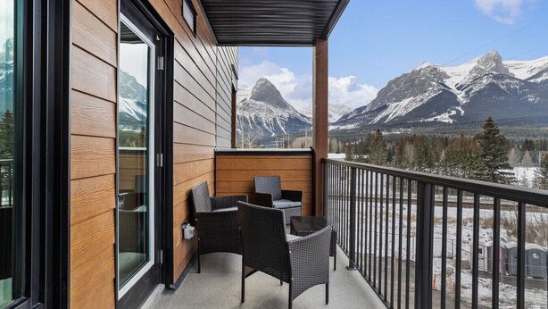 A balcony with wicker furniture, a glass door, and a view of snow-capped mountains. - “The Ascent Mountain Haven” (Canmore)