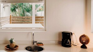 Cocina con ventana que da a una terraza de madera y plantas tropicales. Hay una cafetera y un globo decorativo sobre la encimera.