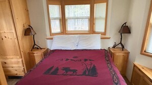 Un dormitorio con cama, dos mesitas de noche, una ventana con persianas y un armario de madera.