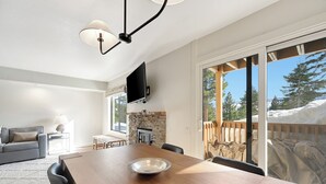 A dining area with a wooden table, chairs, and a large bowl. A flat-screen TV is mounted on the wall above the table. - Discovery 4 111:Near Canyon Lodge, Dog Friendly (Mammoth Lakes)