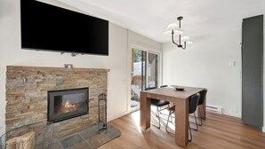 A modern living room with a stone fireplace, a flat-screen TV, a dining table with chairs, and a chandelier. - Discovery 4 111:Near Canyon Lodge, Dog Friendly (Mammoth Lakes)