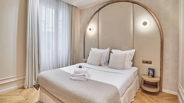 A neatly made bed with a beige headboard, white bedding, and a small bedside table with a lamp and a framed picture. - Suite Air-conditioned Opera-louvre-2 Bedrooms (Paris)