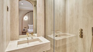 A modern bathroom with a marble sink, a glass shower enclosure, and a mirror reflecting a bedroom with a bed and nightstand. - Suite Air-conditioned Opera-louvre-2 Bedrooms (Paris)