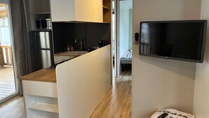 Una cocina moderna con microondas, refrigerador y lavamanos. Hay un televisor montado en la pared y una mesa pequeña con un periódico y control remoto.