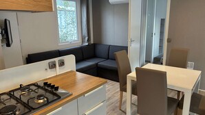 Cocina moderna con estufa a gas, armarios blancos y encimera de madera. Hay un sofá de color oscuro y una mesa de comedor con sillas.