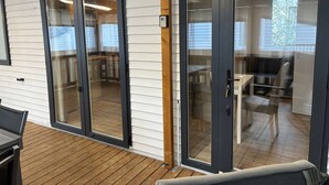 Un interior moderno con una terraza de madera, puertas de vidrio correderas que dan a un comedor y una cocina visible.