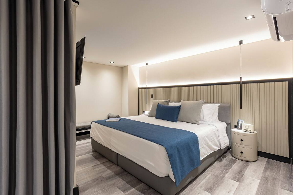 A modern hotel room with a large bed, bedside tables, and a nightstand.