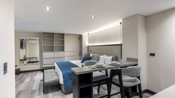 A modern hotel room with a bed, a dining table, and a seating area.