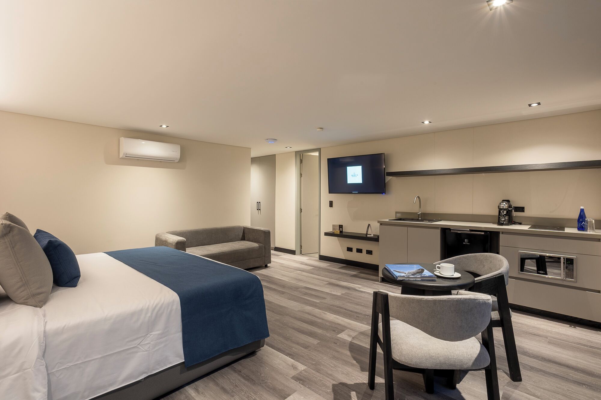 Une chambre d’hôtel moderne comprenant un lit, un canapé, un coin repas avec une table et des chaises, une télévision et une kitchenette.
