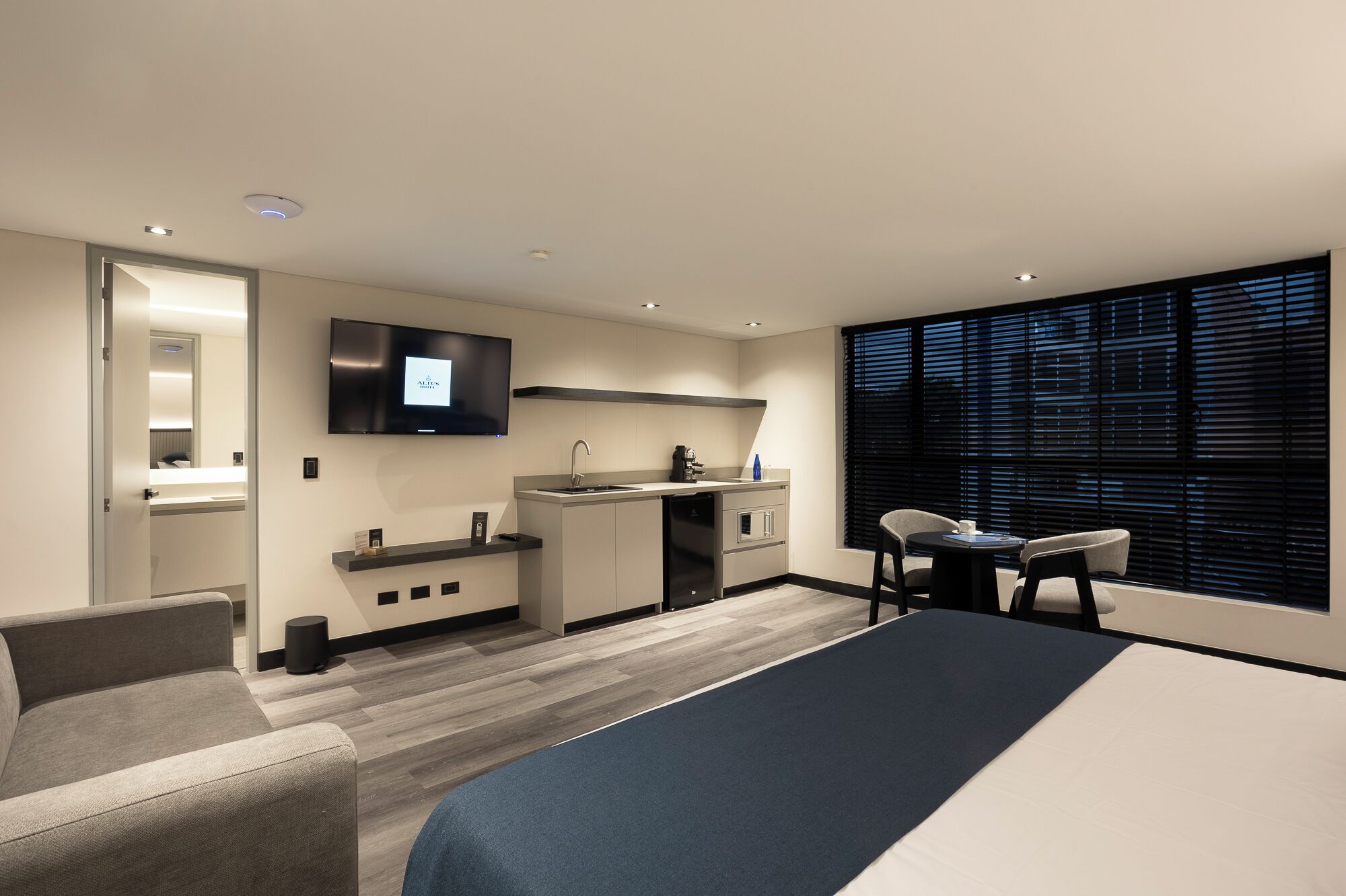 Ein modernes Hotelzimmer mit Bett, Fernseher, Küchenzeile und einer Sitzecke.