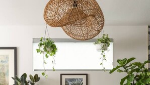 En spiseplads med et rundt træbord, gennemsigtige glasstole og en hængende vævet lampe.