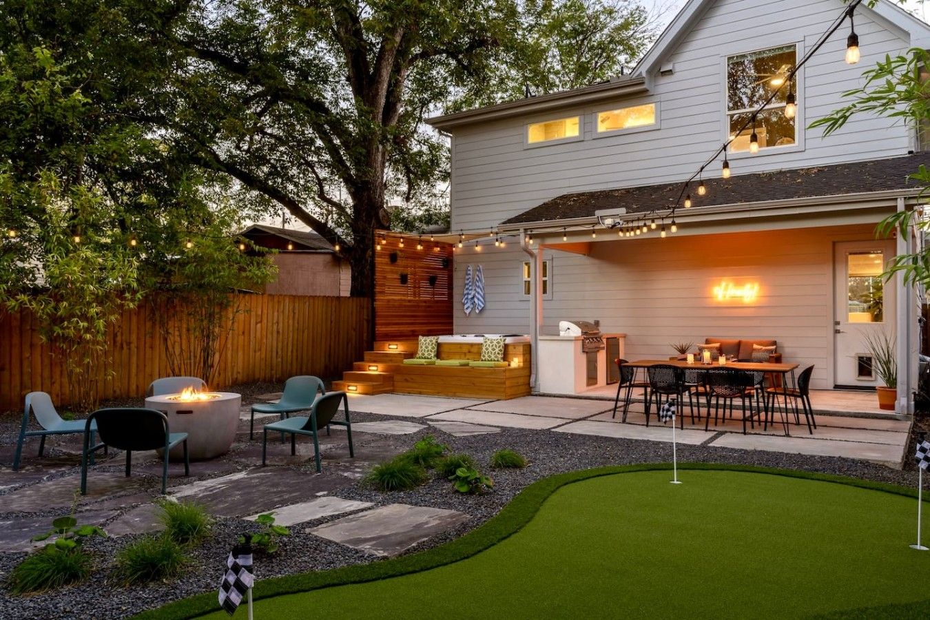 A backyard with a fire pit, outdoor seating, a grill, and a putting green.