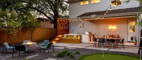 A backyard with a fire pit, outdoor seating, a grill, and a putting green.