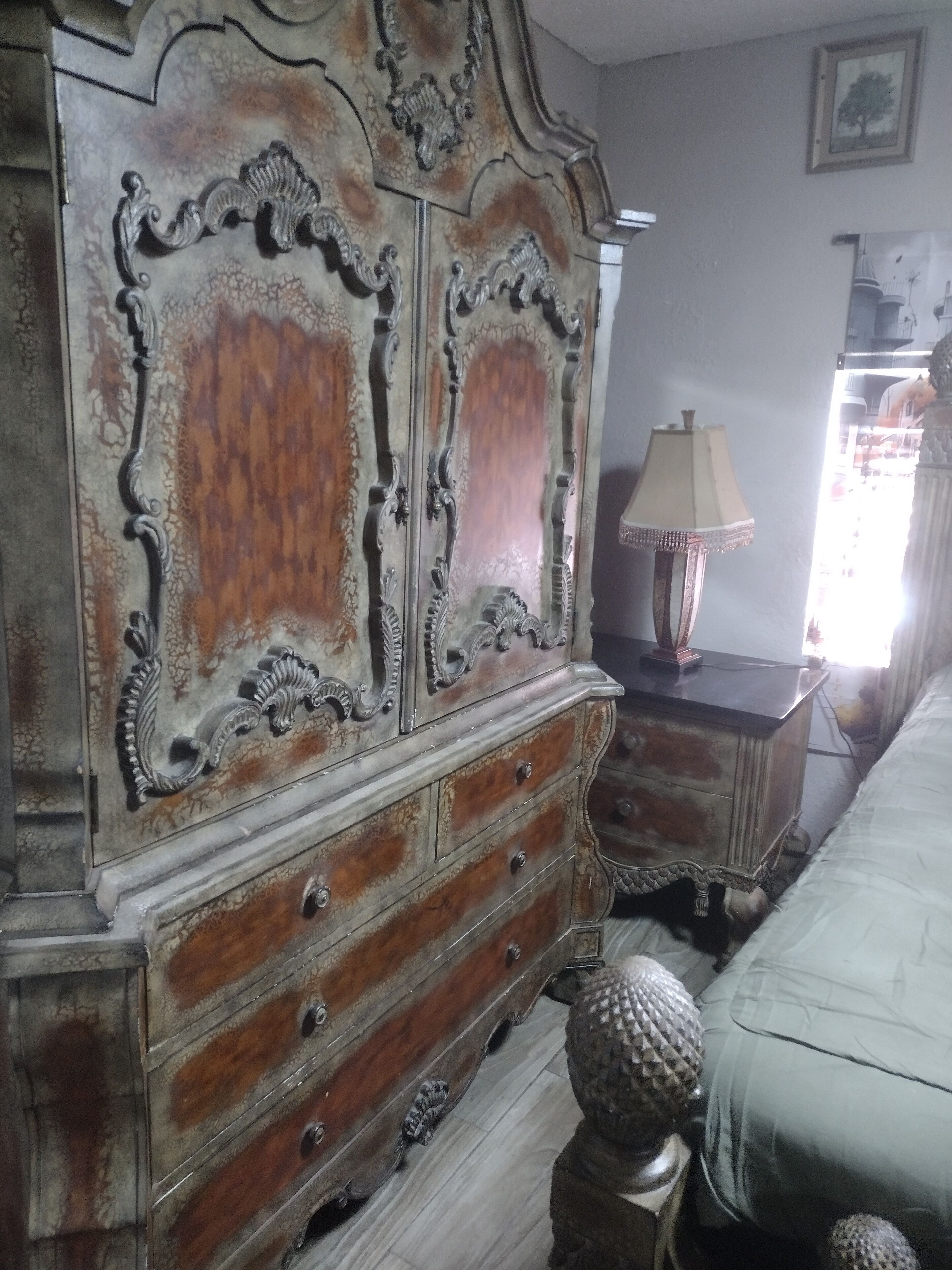 A bedroom with a large wooden dresser, a bedside table with a lamp, and a bed.