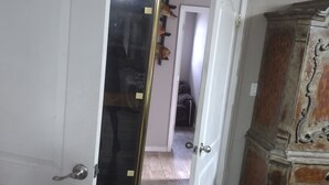 Ein Flur mit einer weißen Tür, einem Holzschrank und einem Spiegel, der einen Teil des Raumes reflektiert.