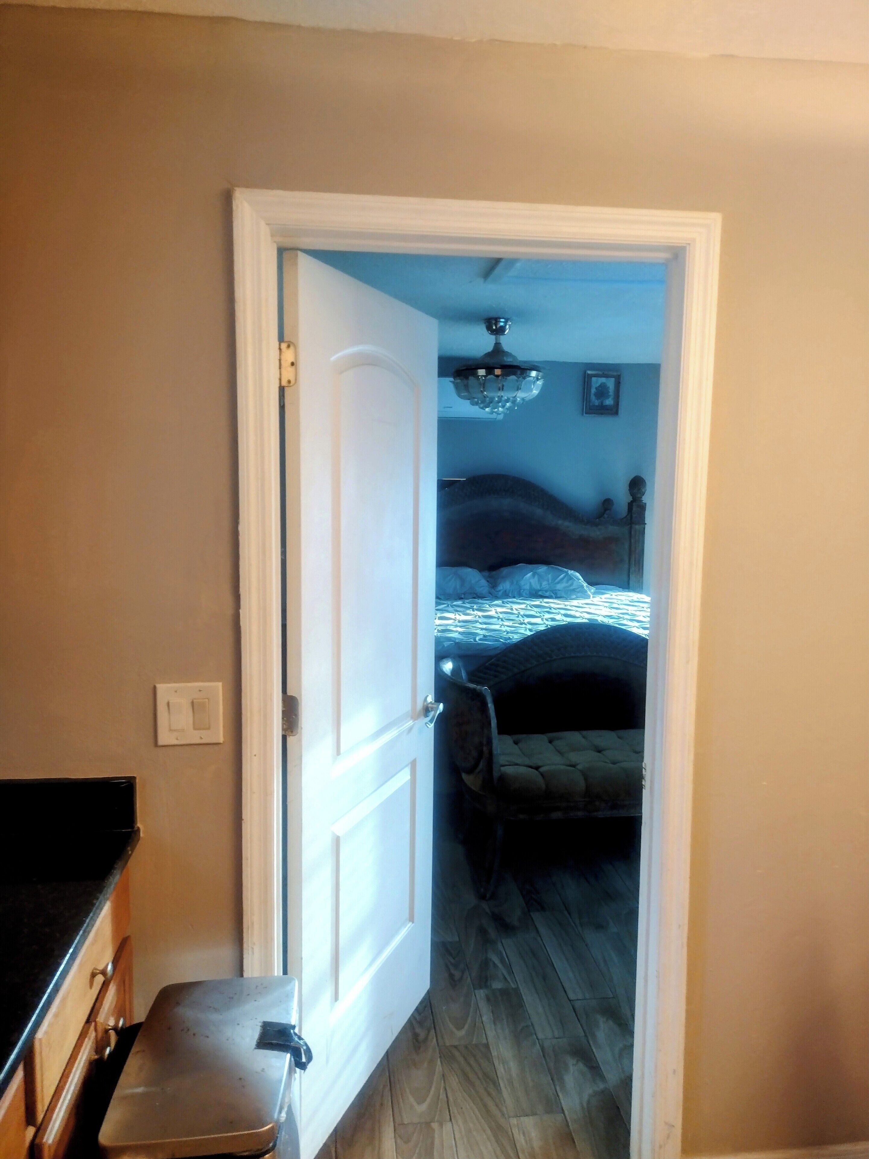 Un pasillo estrecho que conduce a un dormitorio con cama, ventilador de techo y mesita de noche.