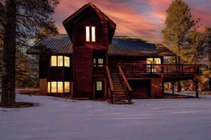 A wooden cabin with a metal roof, a staircase leading to a deck, and a snow-covered ground. - Pah's Haus | Hot Tub | Scenic View | Dog-Friendly (Angel Fire)