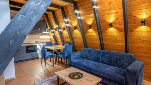 A cozy loft bedroom with a wooden ceiling, a blue sofa, a wooden coffee table, and a dining area with chairs and a table. - Blue Retreat The Golden Cabins With Garden (Gjinar)