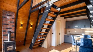 A rustic cabin interior with a wooden staircase, a brick fireplace, and a modern kitchen. - Blue Retreat The Golden Cabins With Garden (Gjinar)
