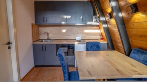 A compact kitchen with grey cabinets, a wooden countertop, and a dining area with a table and blue chairs. - Blue Retreat The Golden Cabins With Garden (Gjinar)