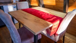 A wooden table with a red cloth, surrounded by cushioned chairs in a cabin-style room with wooden walls and a small kitchenette in the background. - Grey Retreat The Golden Cabins With Garden (Gjinar)