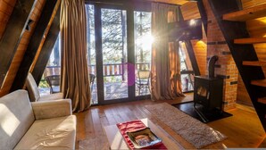 A cozy room with a wooden ceiling, a sofa, a fireplace, and a large window with curtains. - Grey Retreat The Golden Cabins With Garden (Gjinar)