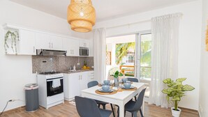 A modern kitchen with white cabinets, a gas stove, and a microwave. There is a dining table with chairs and a potted plant. - Luxury 1BR Paraiso Bayahibe · Pool · Beach · AC · Kitchen (Bayahíbe)