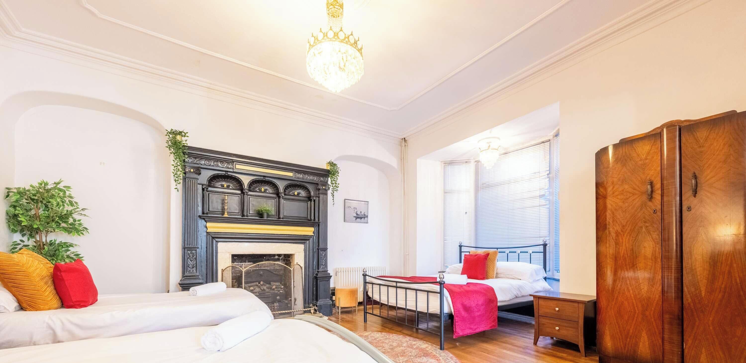 Une chambre avec une cheminée, deux lits, une armoire et un lustre.