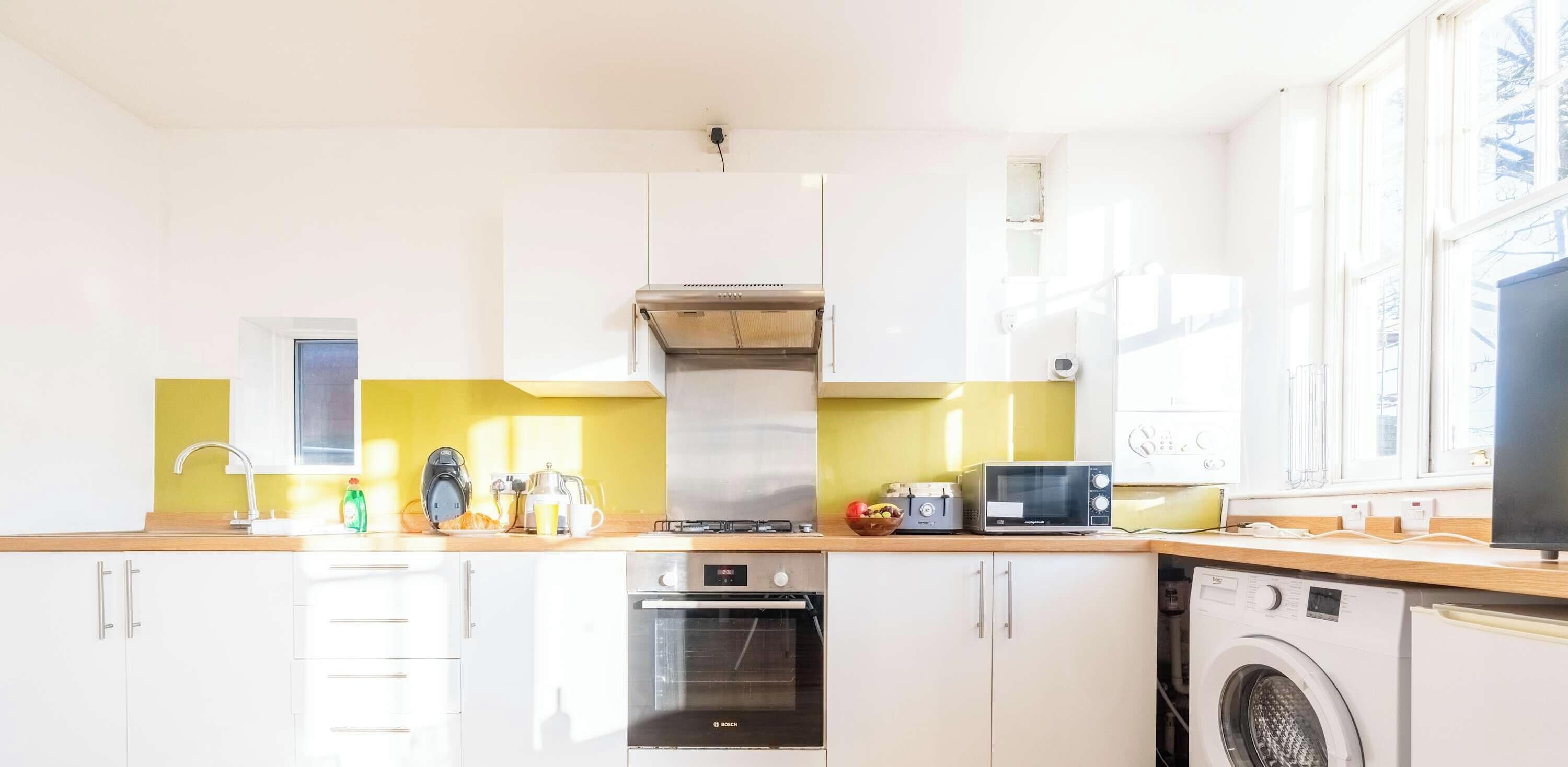 Una cocina moderna con armarios blancos, una campana extractora de acero inoxidable, un horno Bosch, un microondas y una lavadora.