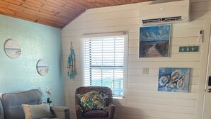 A cozy living room with a wooden ceiling, a gray sofa, a wicker chair, a round table, and a window with blinds. - Welcome to The Crow's Nest at Fisherman's Wharf, a cozy waterfront 1 bedroom. (Cedar Key)