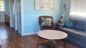 A spacious living area with a wooden ceiling, a round table, a blue sofa, and a chair with a colorful cushion. - Welcome to The Crow's Nest at Fisherman's Wharf, a cozy waterfront 1 bedroom. (Cedar Key)