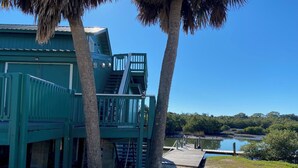A green building with a staircase leading to a deck overlooking a body of water. - Welcome to The Crow's Nest at Fisherman's Wharf, a cozy waterfront 1 bedroom. (Cedar Key)