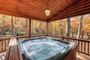Un bain à remous dans un gazebo en bois, avec vue sur les arbres aux couleurs automnales.