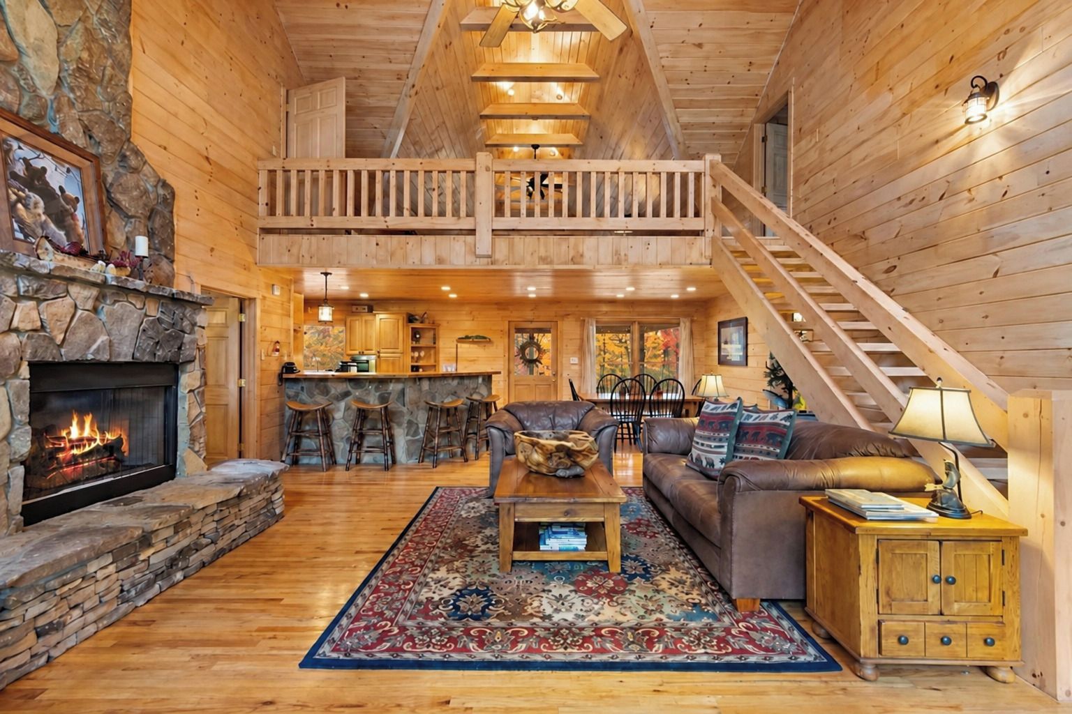 A spacious log cabin interior with a stone fireplace, a dining area, a living room with a sofa and coffee table, and a staircase leading to an upper level.