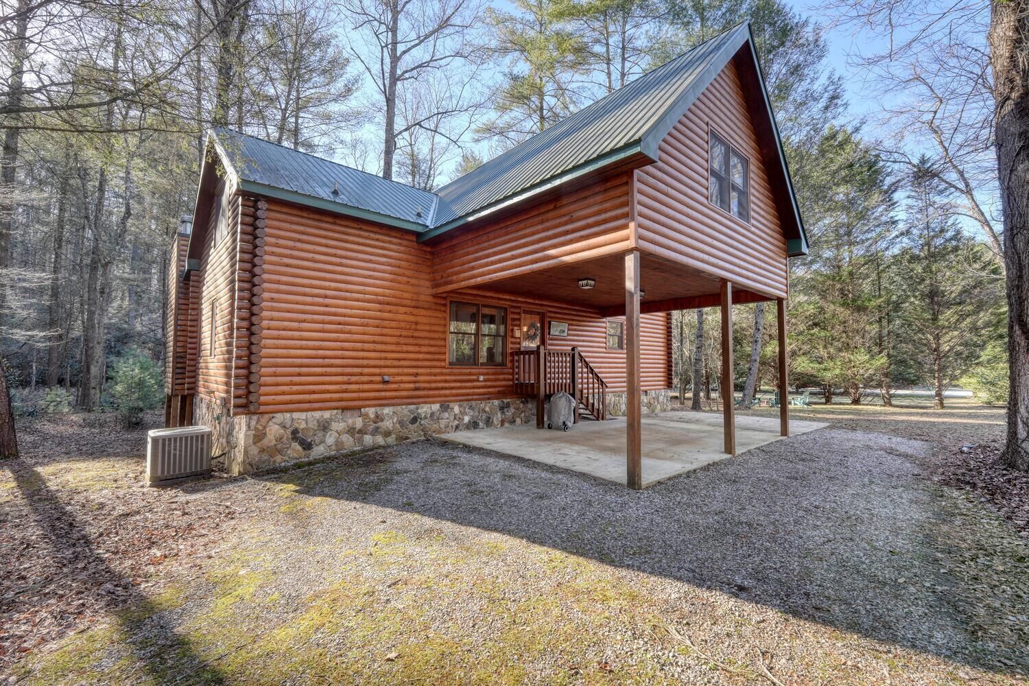 A log cabin with a stone foundation, a covered porch, and a staircase leading to the entrance.