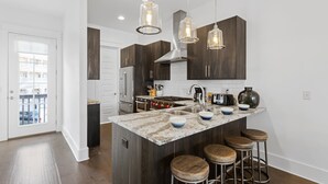 A modern kitchen with dark wood cabinets, a granite island with stools, stainless steel appliances, and pendant lighting. - Seacrest, Steps to Beach & Pools! 4 Bikes Included, Pet Friendly! (Rosemary Beach)