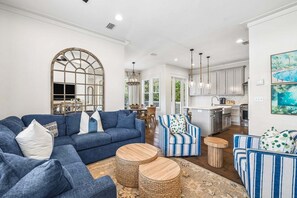 A spacious living room with a blue sofa, a striped armchair, and a dining area with a chandelier. - Outdoor Oasis! Walk 2 Shops & Eat! LSV/Golf Cart, 3 Kings & Bikes! (Santa Rosa Beach)