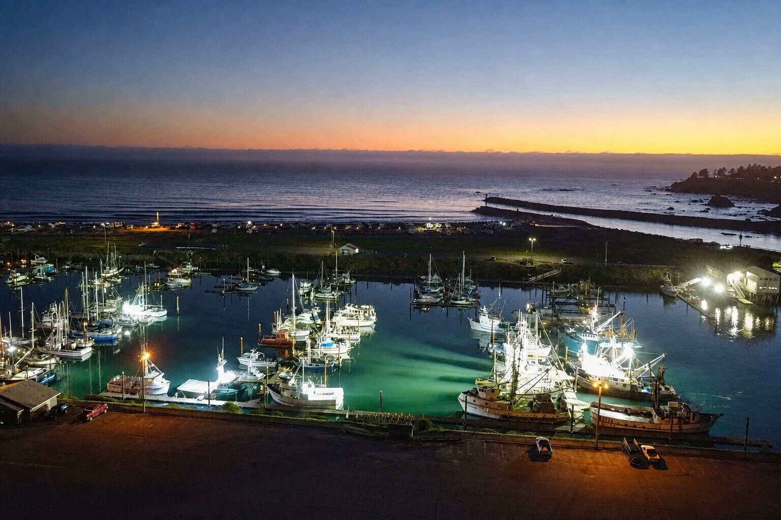 A marina at dusk with boats docked and a sunset in the background.