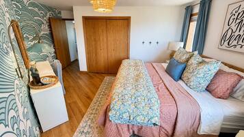A bedroom with a bed, a wooden wardrobe, a nightstand, a lamp, and a wall with a decorative sign.