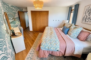 Quarto com cama, guarda-roupa de madeira, mesa de cabeceira, abajur e um quadro decorativo na parede.