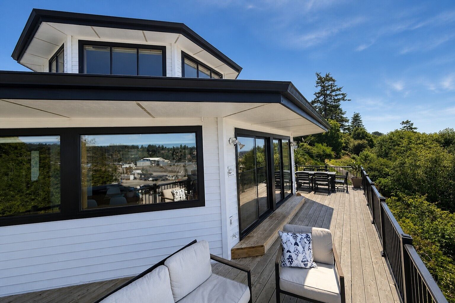 A modern house with a deck, large windows, and a view of the surrounding area.