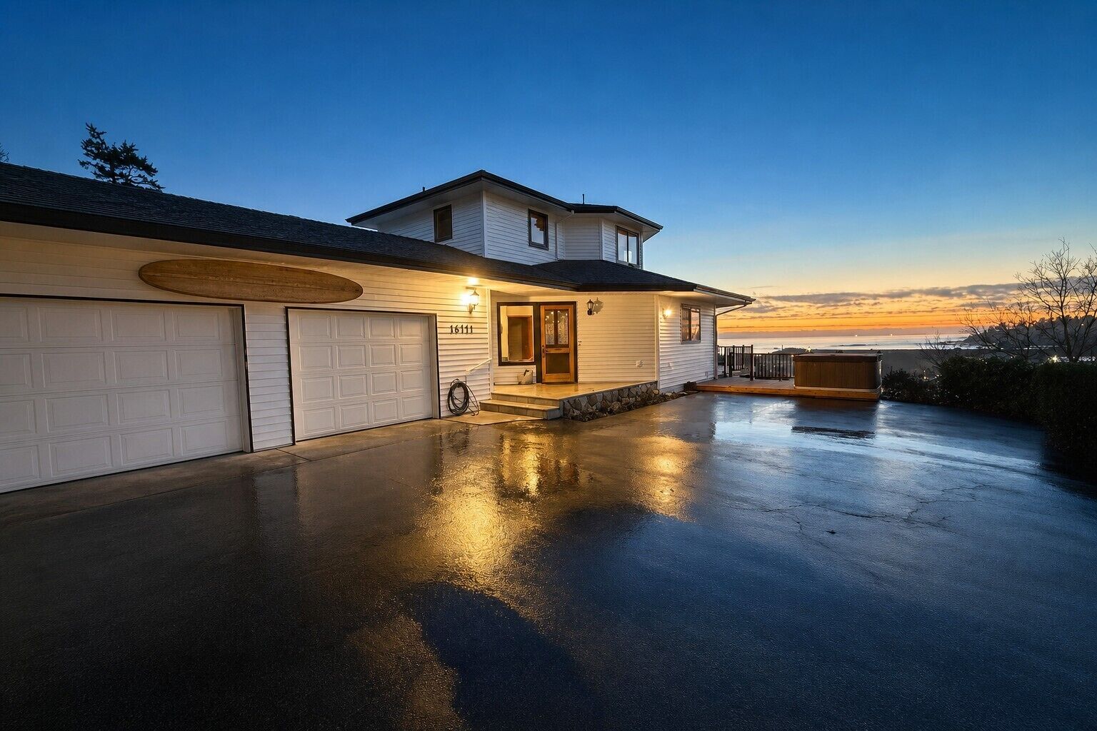 A residential property with a garage, a covered driveway, and a view of the ocean at sunset.