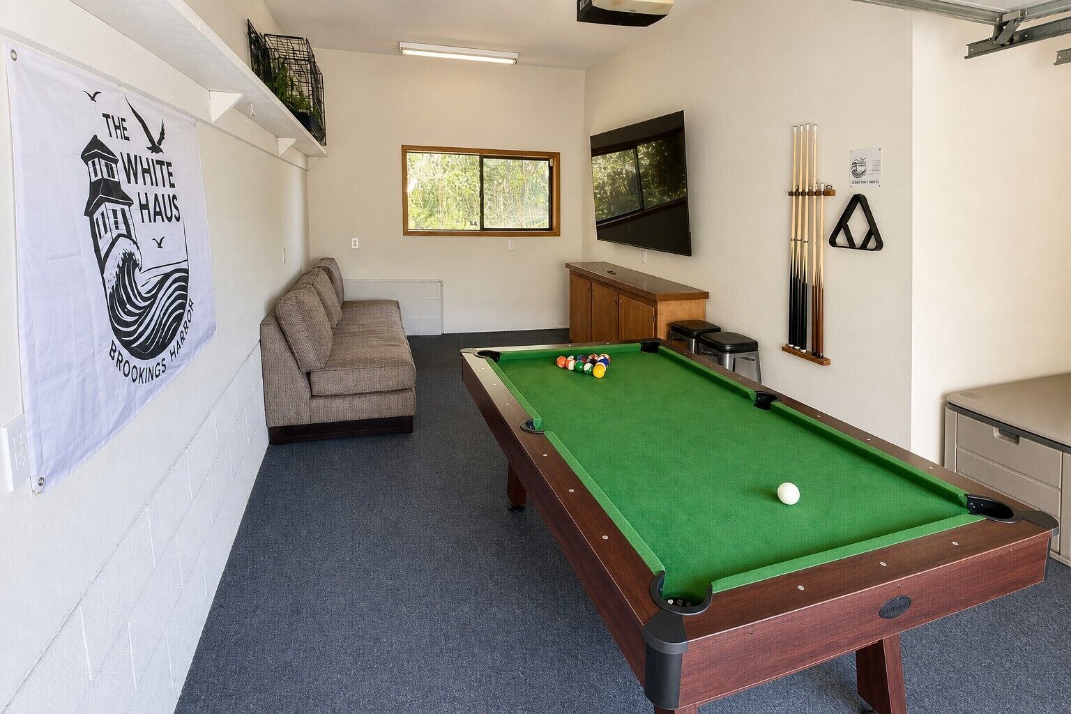 Ein Billardtisch mit Kugeln, eine Couch, ein Fernseher und ein Schild an der Wand.