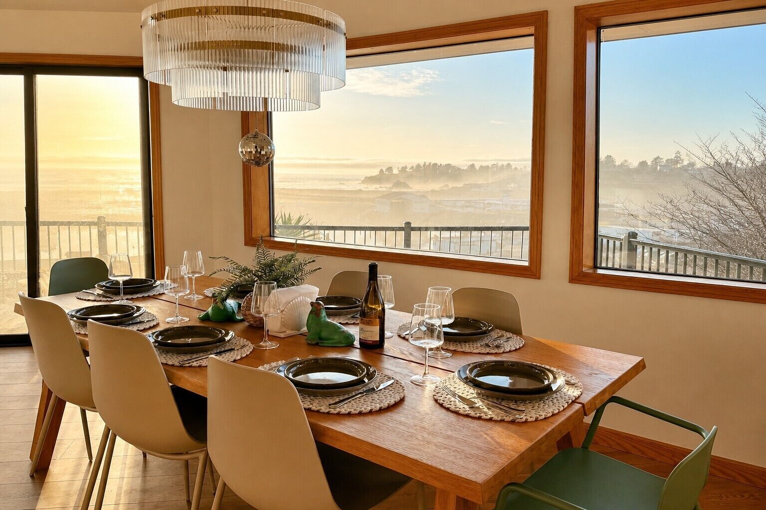 A dining area with a wooden table set for four, large windows with a view, and a chandelier.