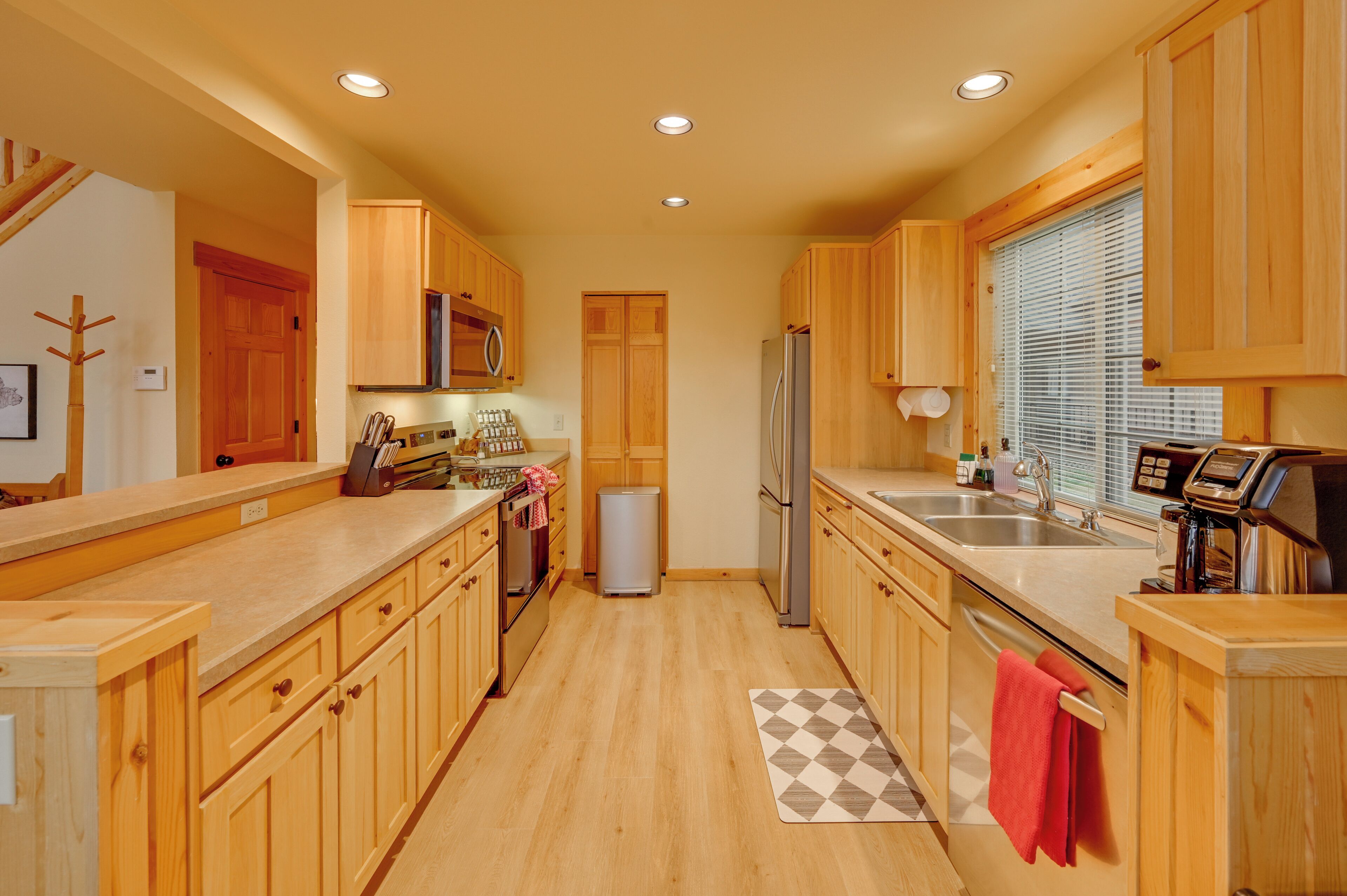 A modern kitchen with wooden cabinets, stainless steel appliances, and a checkered rug.
