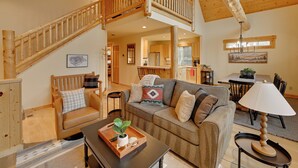 A spacious living area with a wooden staircase, a sofa set, a dining table, and a kitchen in the background. - Game Room & 5 Pools: Chalet at Eagle Crest Resort (Redmond)