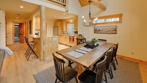 A spacious dining area with a long wooden table and chairs, a kitchen in the background, and a wooden staircase leading to an upper level. - Game Room & 5 Pools: Chalet at Eagle Crest Resort (Redmond)